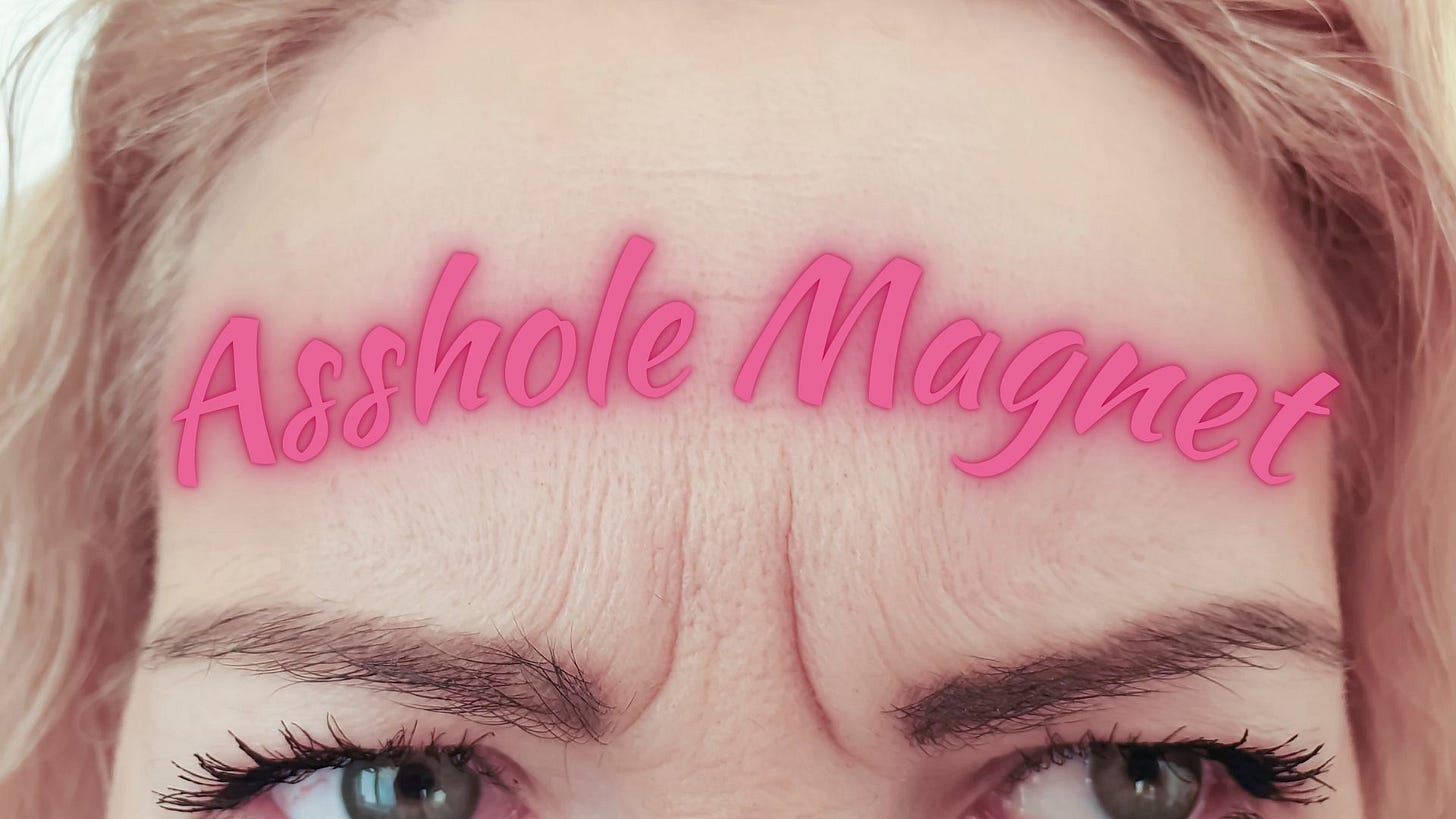 Close-up of a woman’s furrowed forehead with the phrase “Asshole Magnet” written in bright pink, playful script across it, positioned just above her eyebrows. Her intense eyes are looking to the side, adding emphasis to the humorous and bold message.
