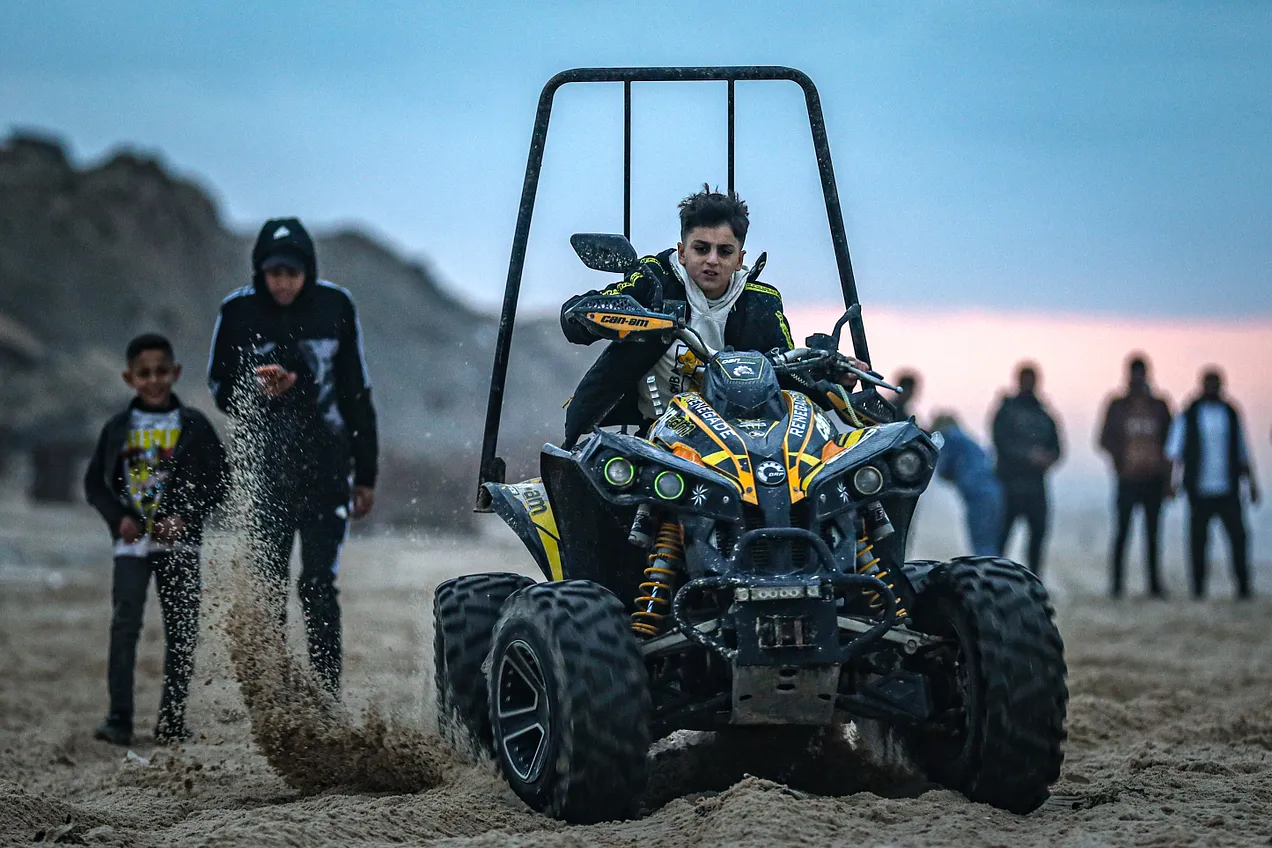 모래사장에서 사륜 자동차를 타고 있는 사람. 앞의 사진들에 비해 어린, 청소년으로 보이는 이가 주인공이다. 주위도 사람 몇이 서 있다.