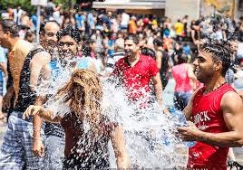 Celebratin of Vardavar in Armenia, group of people throwing wter on one another, with man in red shirt smiling and woman with long-hair being drenched