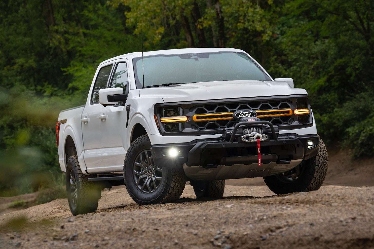A white 2024 Ford F-150 Tremor is parked in the dirt, equipped with a new bumper and a Warn winch.