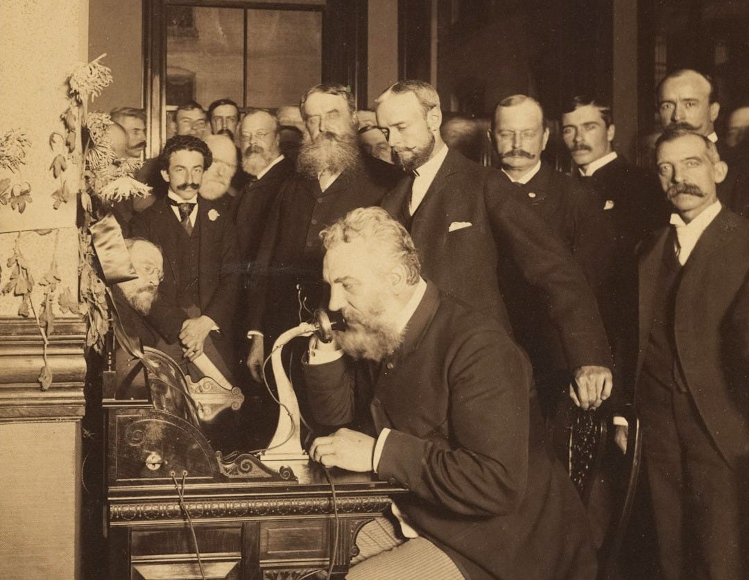 Men gathered around alexander graham bell using the telephone