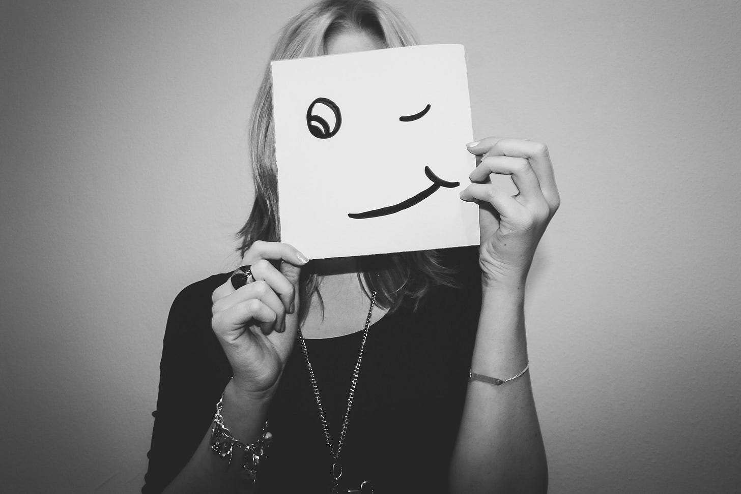 Woman holding a sign to hide her face. The sign is a smiling face drawn on paper. Woman holding a sign to hide her face. The sign is a smiling face drawn on paper.