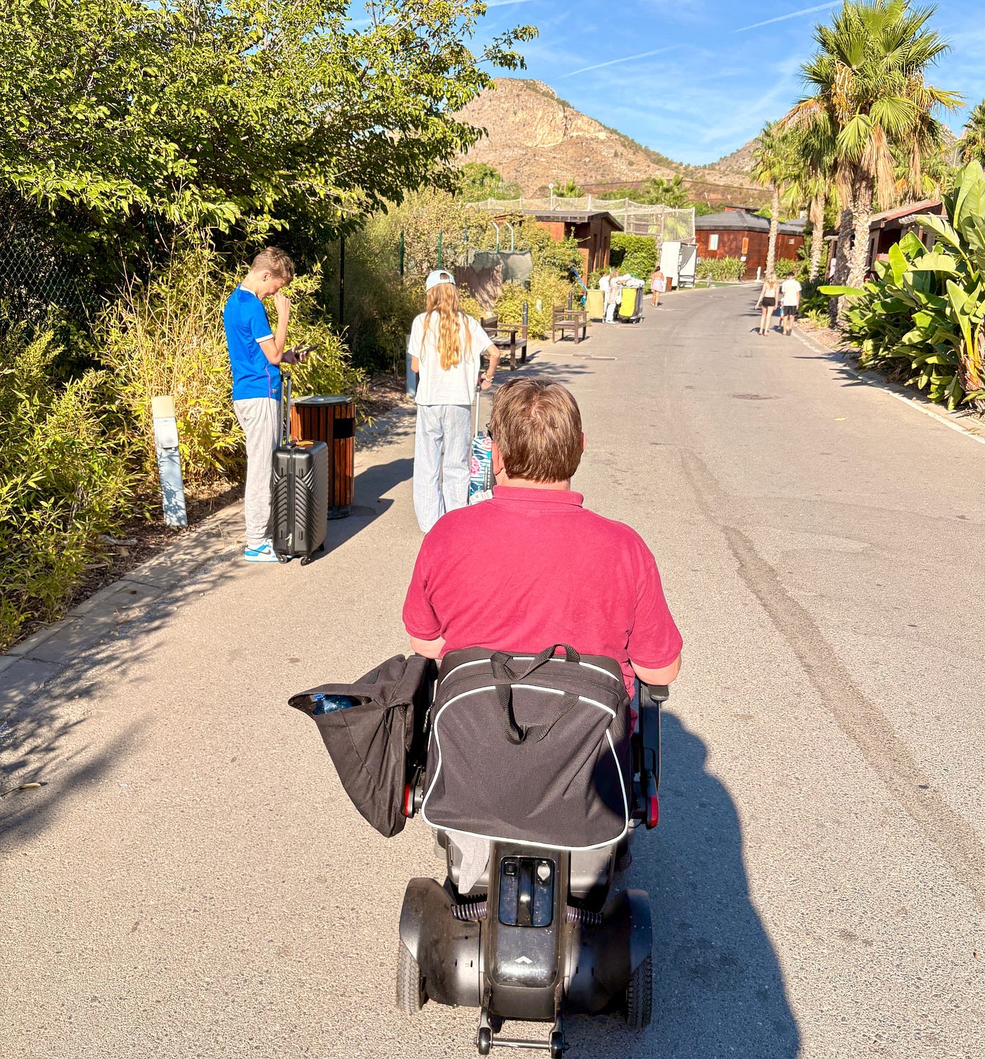 The author in his wheelchair with others up ahead wheeling suitcases.