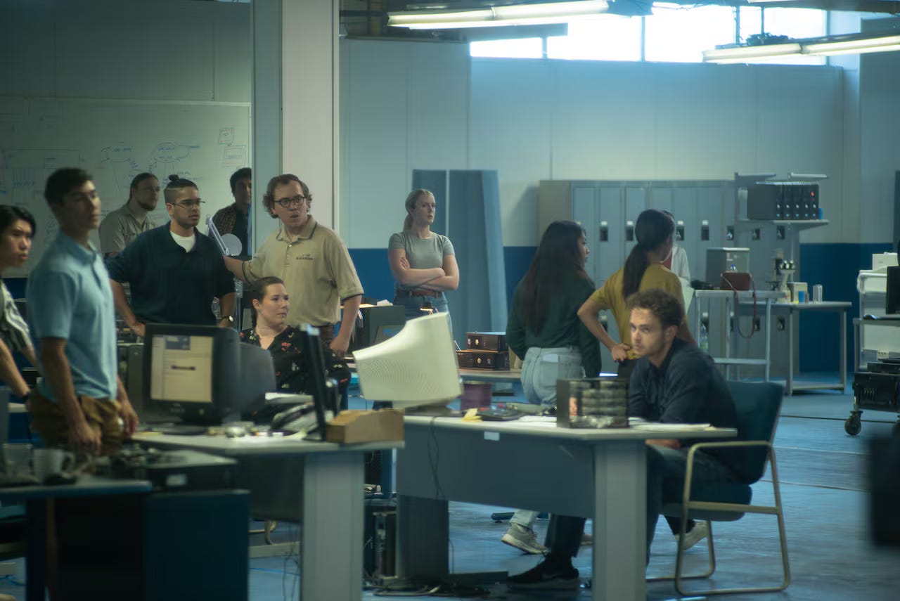 A team of people in a busy startup office looking at monitors and whiteboards.