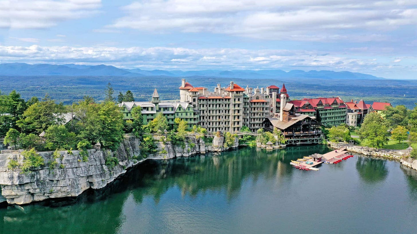 Aerial view of Mohonk Mountain House with acres of forest behind it, glacial lake in front of it.