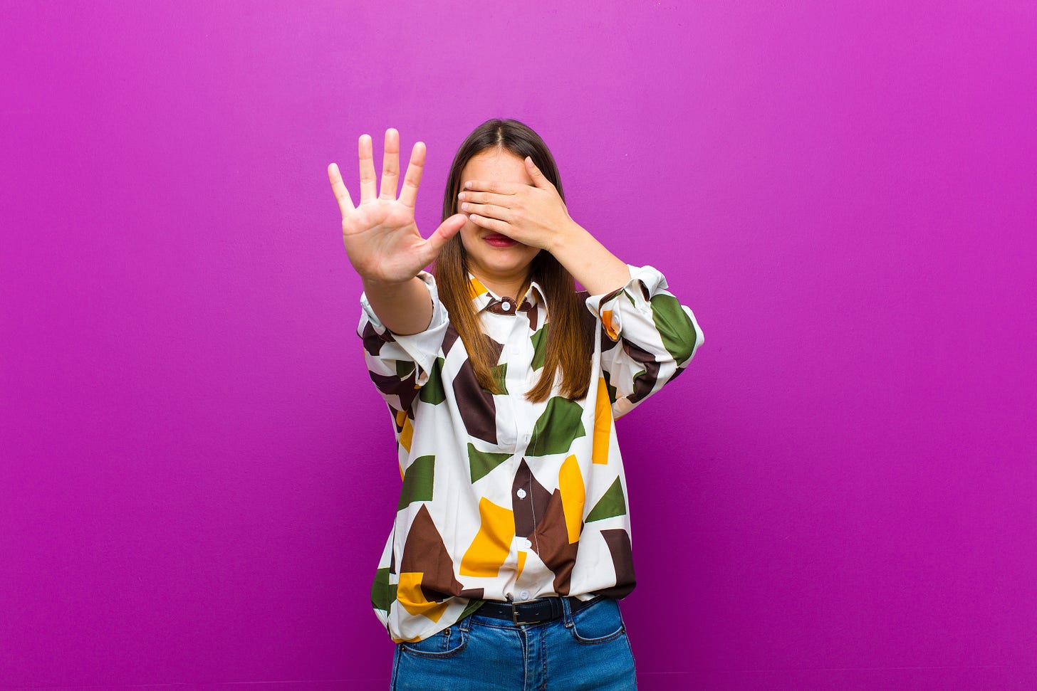 Woman with hand over her eyes and other hand saying Stop