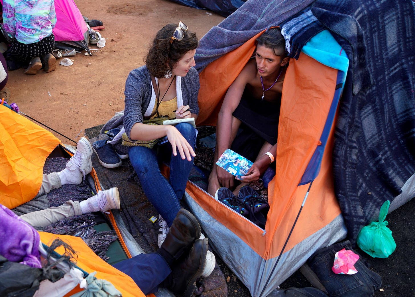 A woman journalist sits outside a tent and speaks with a young man who sits inside the tent A woman journalist sits outside a tent and speaks with a young man who sits inside the tent