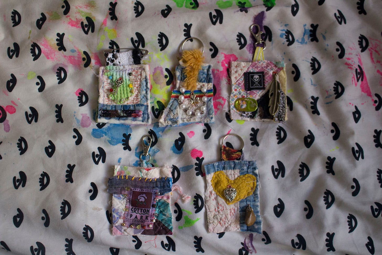 five cloth keychains with beads and charms sewn onto them