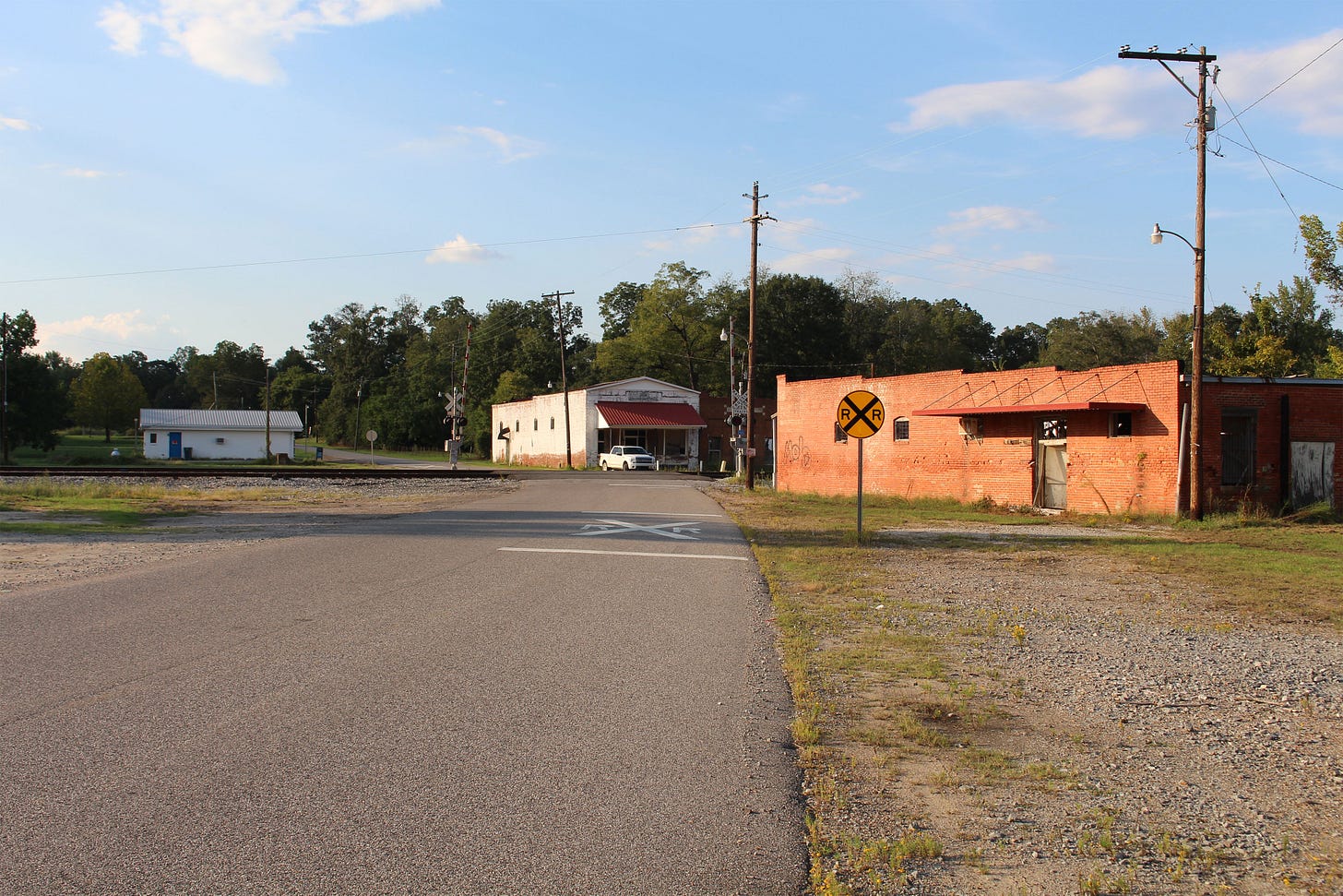 The train crossing of a rural road surrounded by three low buildings. The train crossing of a rural road surrounded by three low buildings.