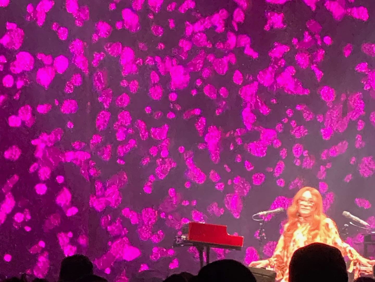 photo of tori amos playing a piano and keyboard in front of bright magenta lights against a backdrop