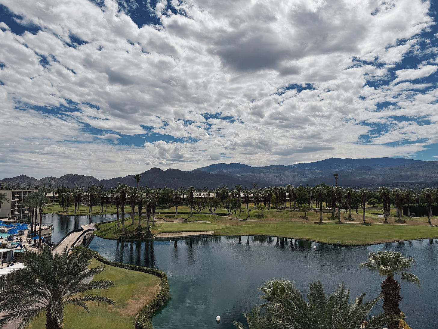 View from JW Marriott Desert Springs across a pond and golf course toward palm trees and the San Jacinto Mountains under a cloudy sky. View from JW Marriott Desert Springs across a pond and golf course toward palm trees and the San Jacinto Mountains under a cloudy sky.