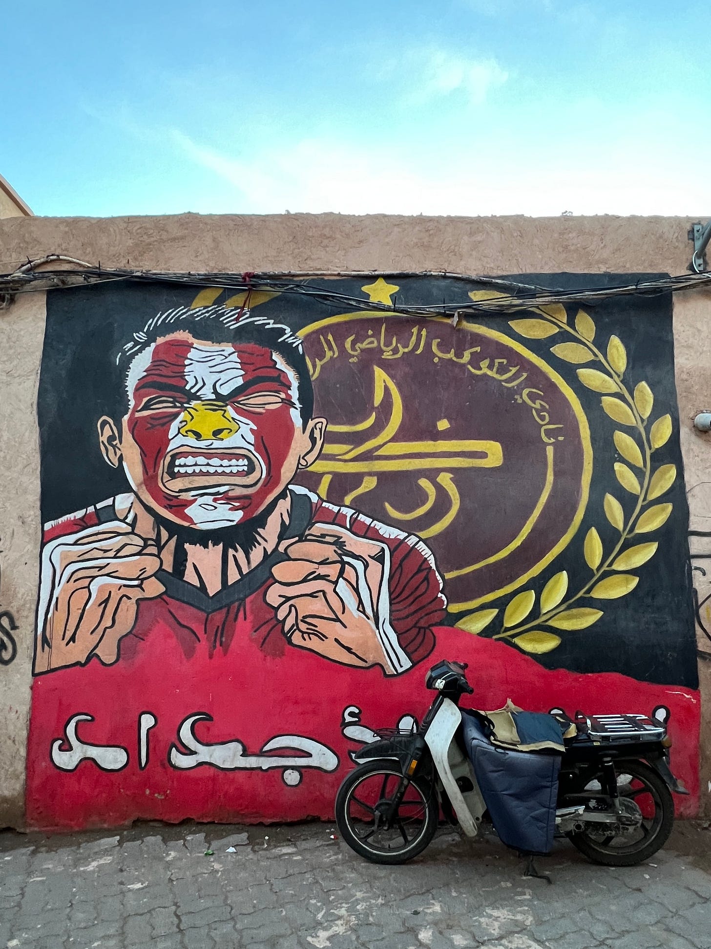 Football mural celebrating local club KACM on a wall in Marrakech, with a parked moped in front.