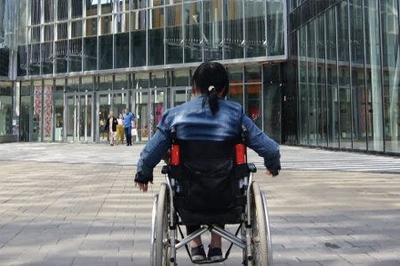 Une jeune femme en fauteuil roulant devant une tour de bureaux Une jeune femme en fauteuil roulant devant une tour de bureaux