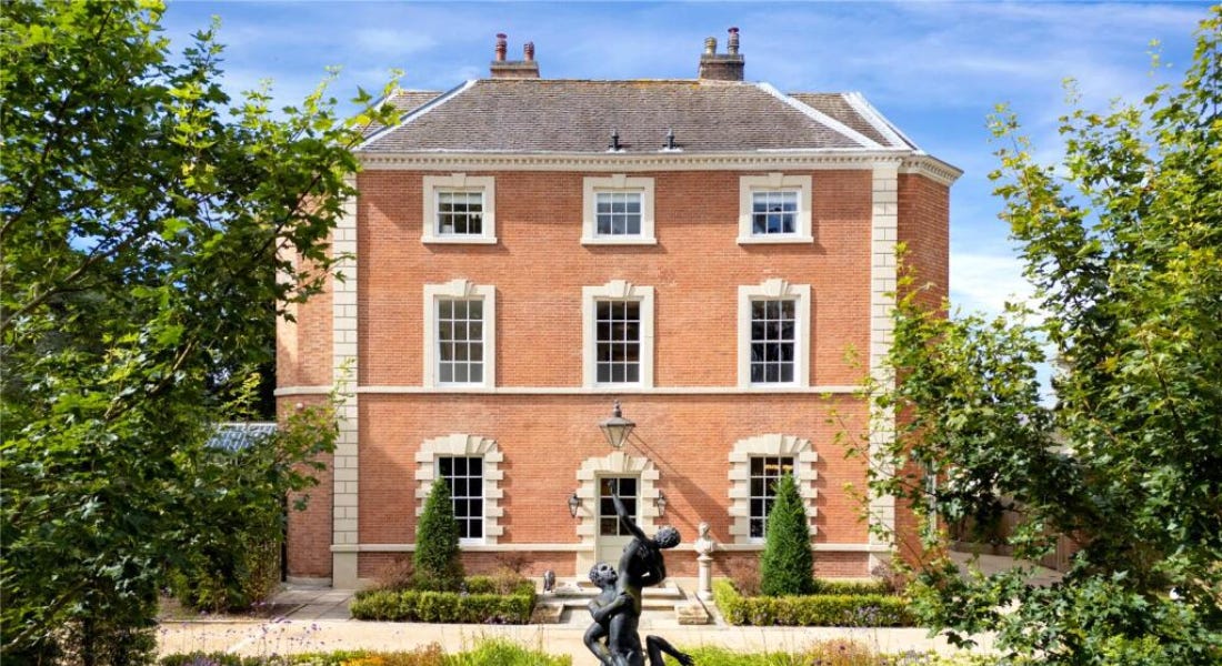 A large brick home with white brick detailing, with a statue in front of it and trees around it