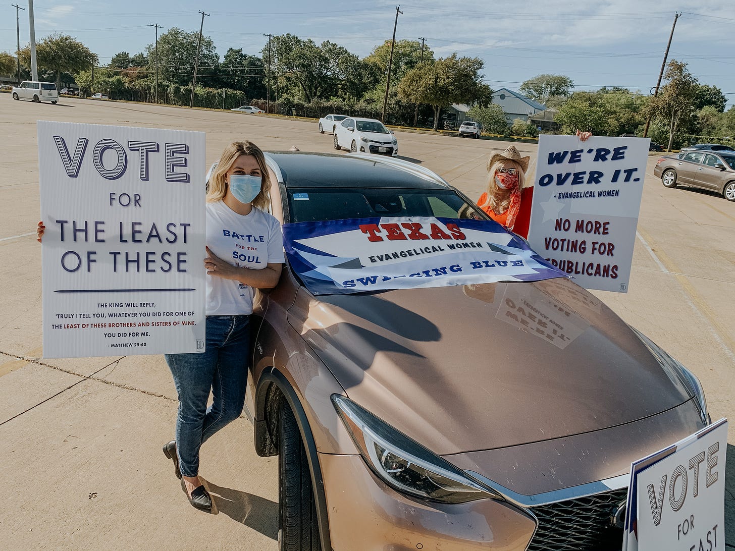 Two women stand in a parking lot holding political signs.