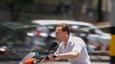 A man in a white shirt sits on a motorbike looking serious as it speeds past blurred scenery