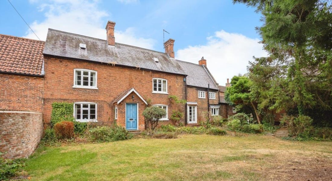 A brick farmhouse with a blue door and a lawn and a tree in front of it