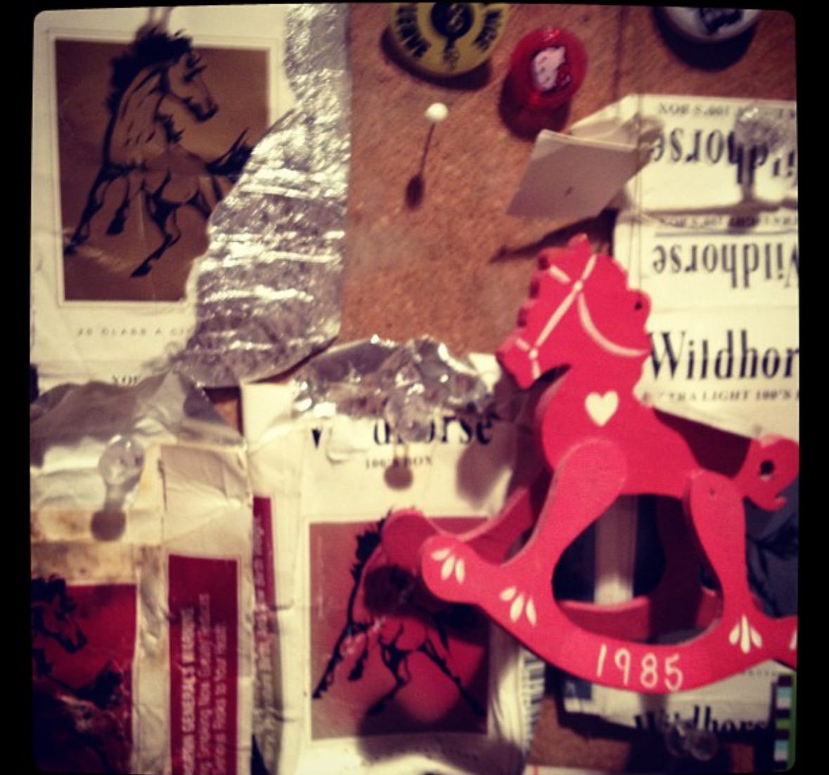 bulletin board tacked with found and torn cigarette packs of Wild Horse and an rocking horse ornament bulletin board tacked with found and torn cigarette packs of Wild Horse and an rocking horse ornament