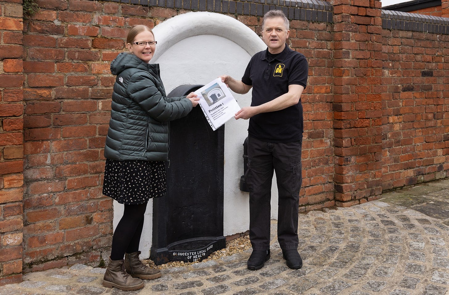 A picture of two people standing in front of a black water tap holding the paper petition together. A picture of two people standing in front of a black water tap holding the paper petition together.