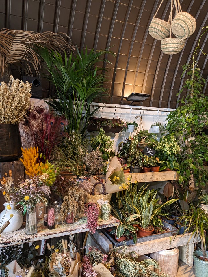 Image one, a brown bag with a bouqet of flowers on the ground between a pair of white trainers. Image two, a image of flowers and dried flowers in a shop.