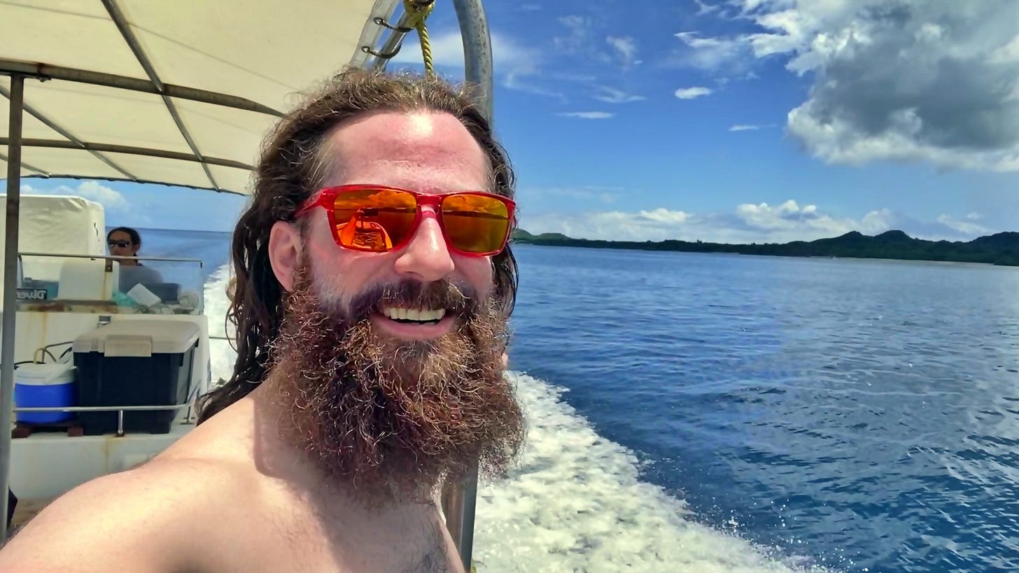 Matt Ketchum wearing red Oakley sunglasses and no shirt, long hair and beard out in the wind, on a boat in Ishigaki, Okinawa, Japan diving.