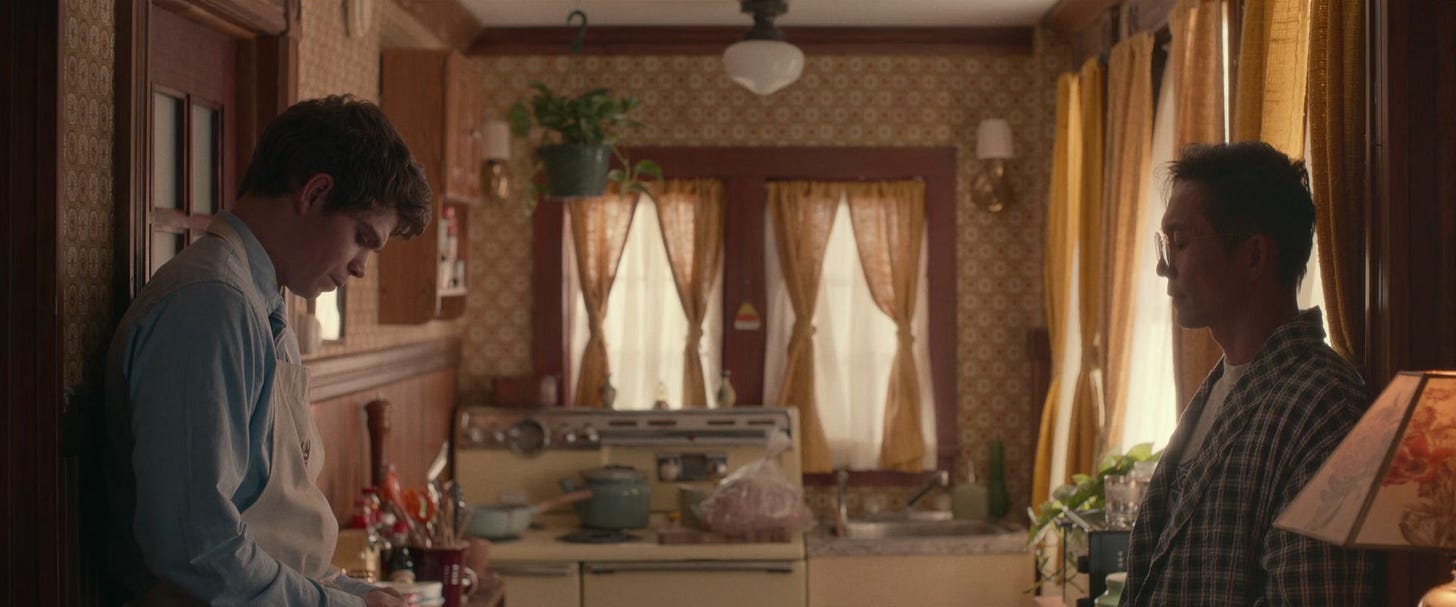 A still from the film 'The Half of It'. Paul and Colin stand in the kitchen of Colin and Ellie's house. Colin is in his dressing gown. Paul wears a white apron over his blue button-up shirt. The kitchen has a 1970s feel to it and is mostly yellow. A still from the film 'The Half of It'. Paul and Colin stand in the kitchen of Colin and Ellie's house. Colin is in his dressing gown. Paul wears a white apron over his blue button-up shirt. The kitchen has a 1970s feel to it and is mostly yellow.