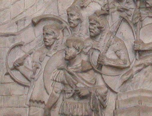 A close-up profile view of the historical bronze relief detail from Trajan's Column depicting a group of Roman legionaries, including cornicines (military musicians) holding and blowing into large, curved, G-shaped bronze horns called cornua during a military drill.