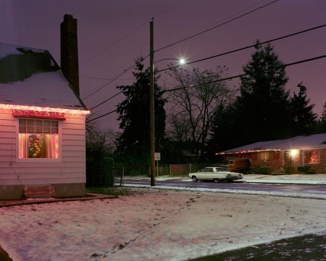 This may contain: a small white house with christmas lights on it's windows in the snow at night