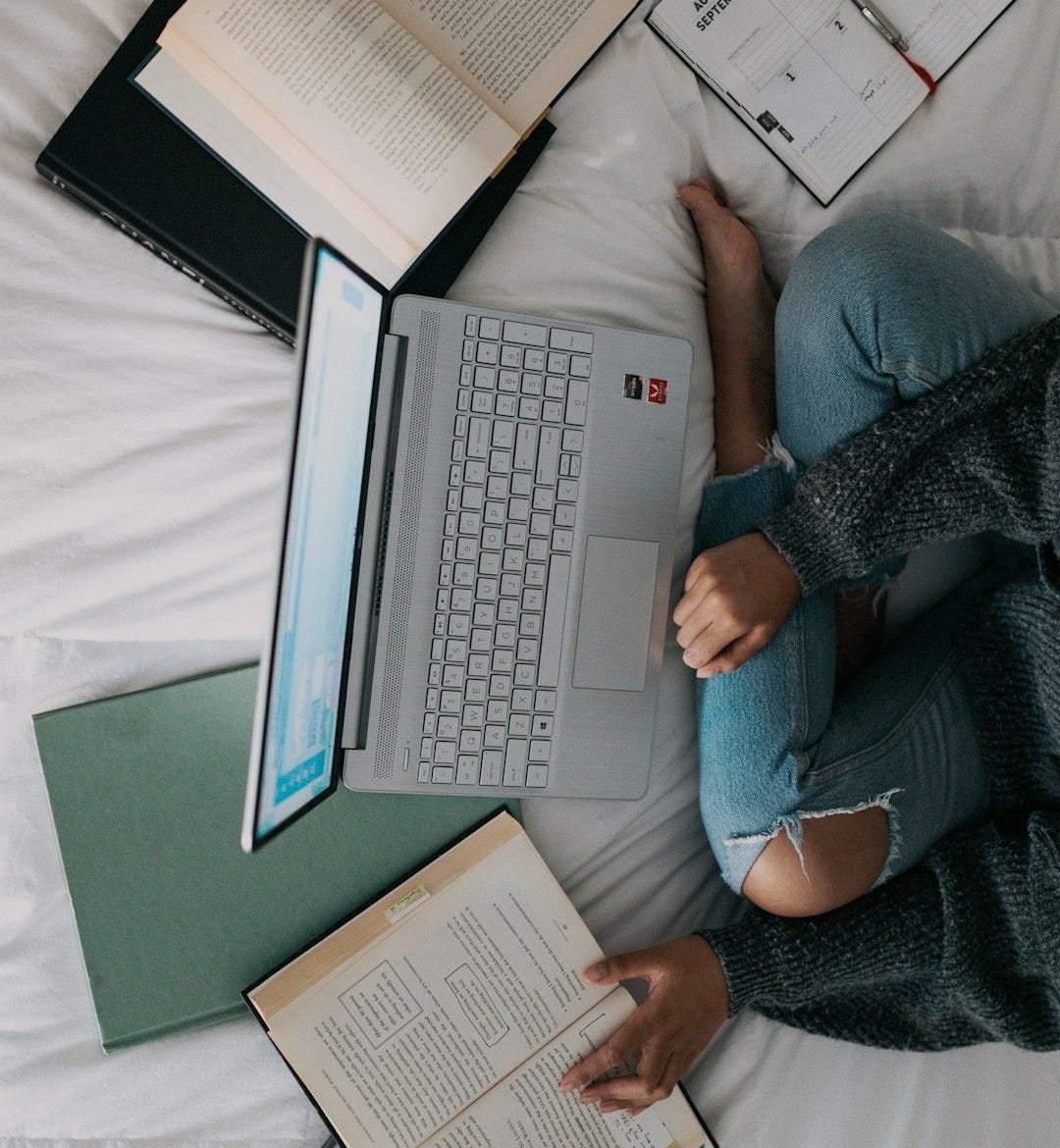 woman in blue long sleeve shirt and blue denim jeans sitting on bed using laptop