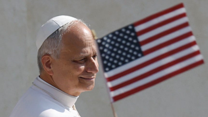 Smiling Pope leo stands in front of the American flag Smiling Pope leo stands in front of the American flag