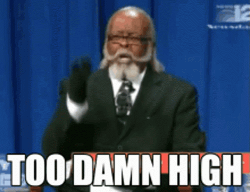 a man in a suit and tie is giving a speech and the words too damn high are above him a man in a suit and tie is giving a speech and the words too damn high are above him