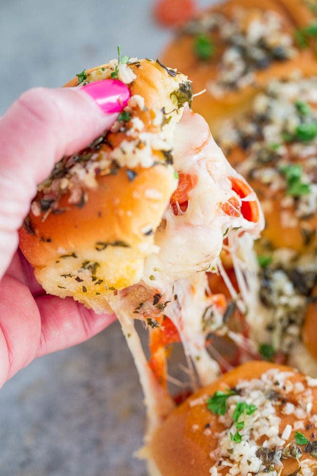 A hand pulling a pepperoni pizza slider from a platter. 