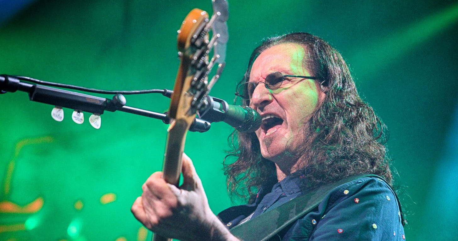 Geddy Lee of Rush playing bass and singing into a microphone on stage.