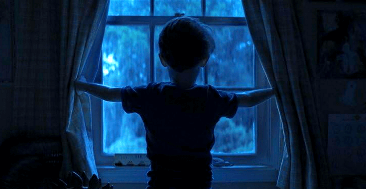 Criança de costas abre as cortinas e encara a janela em meio à luz azulada da noite, sugerindo mistério e expectativa. Criança de costas abre as cortinas e encara a janela em meio à luz azulada da noite, sugerindo mistério e expectativa.