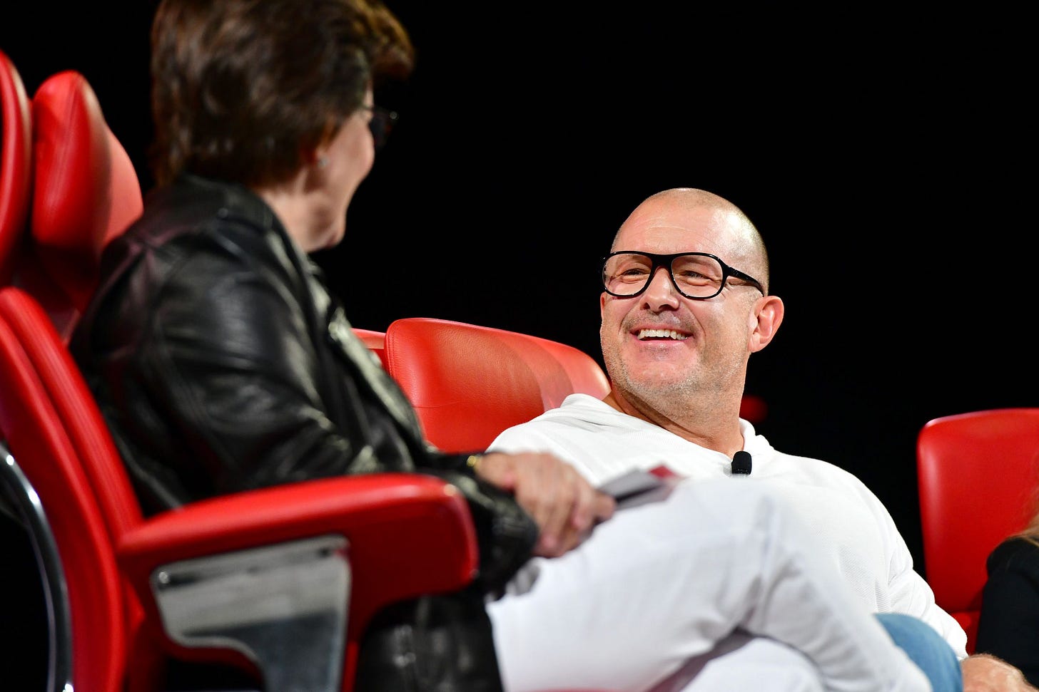 An image of a smiling Jony Ive sitting in a bright red chair. An image of a smiling Jony Ive sitting in a bright red chair.