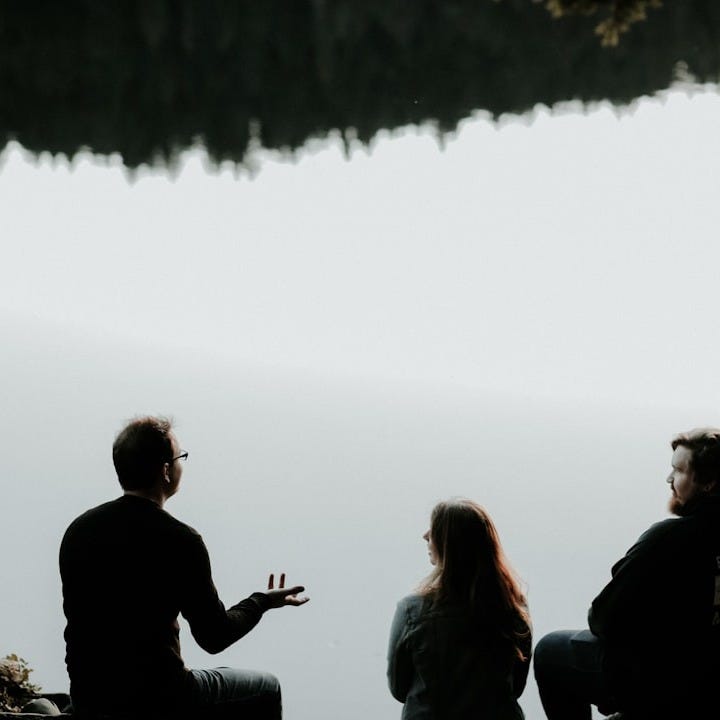 silhouette of three people sitting on cliff under foggy weather