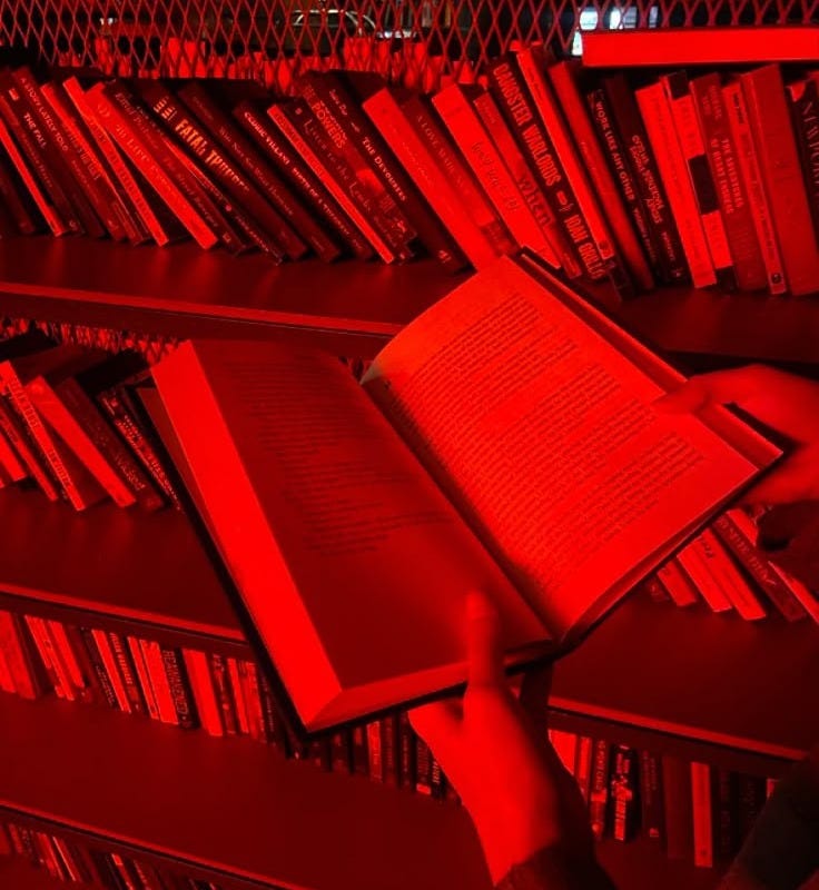 This may contain: a person is holding an open book in front of red bookshelves at night