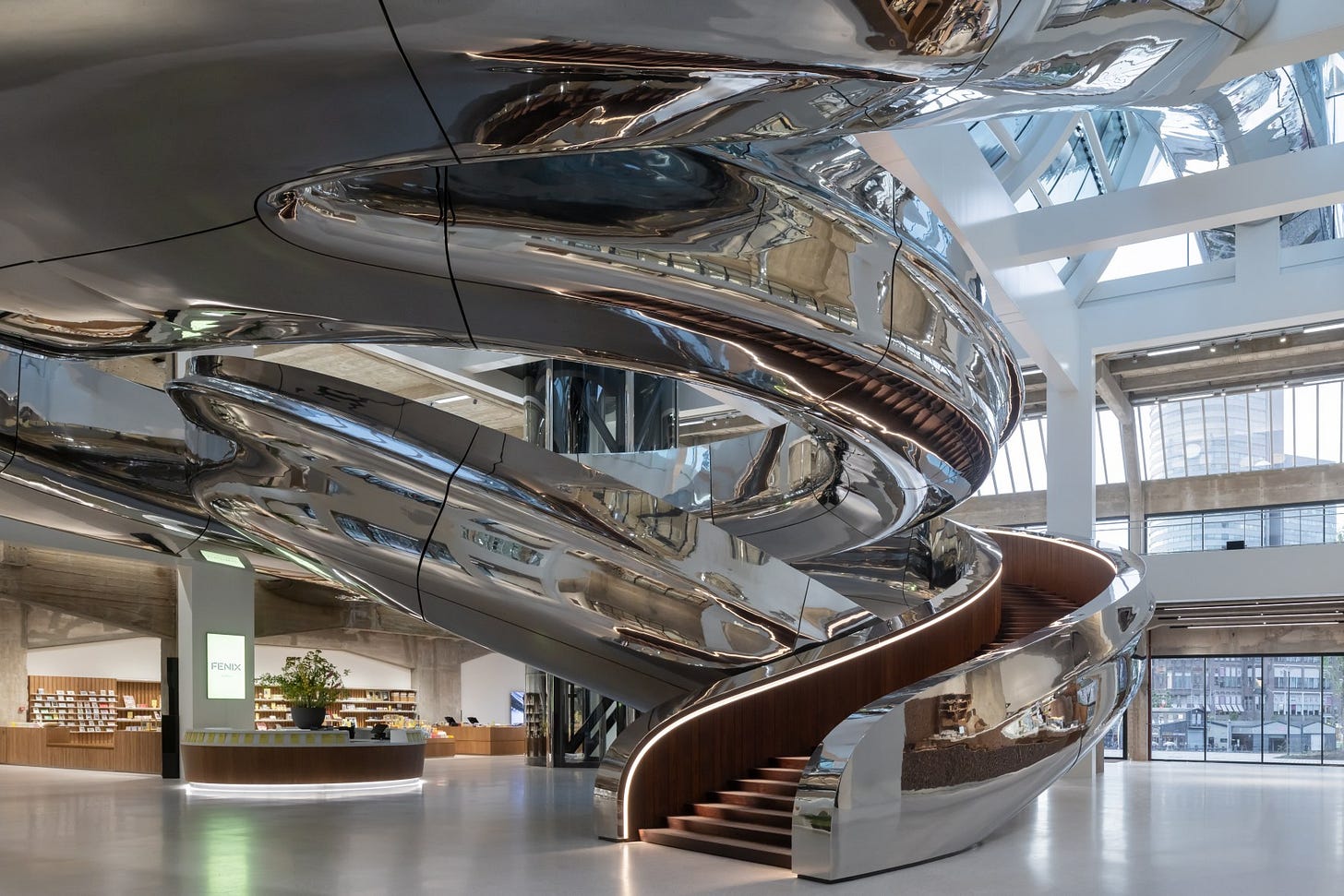 Interior view of FENIX, a new international art museum in Rotterdam, showcasing a large, reflective, metallic staircase.