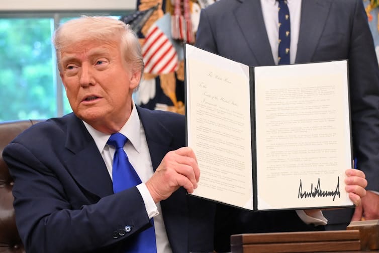 A man in a suit with a blue tie, holding a folder with a white document in it.