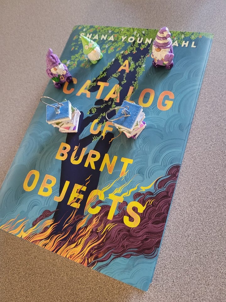 Shana Youngdahl with a sign that says "Welcome Shana Youngdahl" painted with flames, tiny gnomes ontop of the book A Catalog of Burnt Objects by Shana Youngdahl, Shana Youngdahl with a cart of books to sign for students, Shana Youngdahl with the library and a teacher from Centennial High