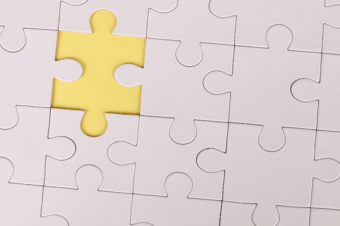 Free Close-up of a white jigsaw puzzle with a single yellow piece missing, symbolizing incompleteness. Stock Photo