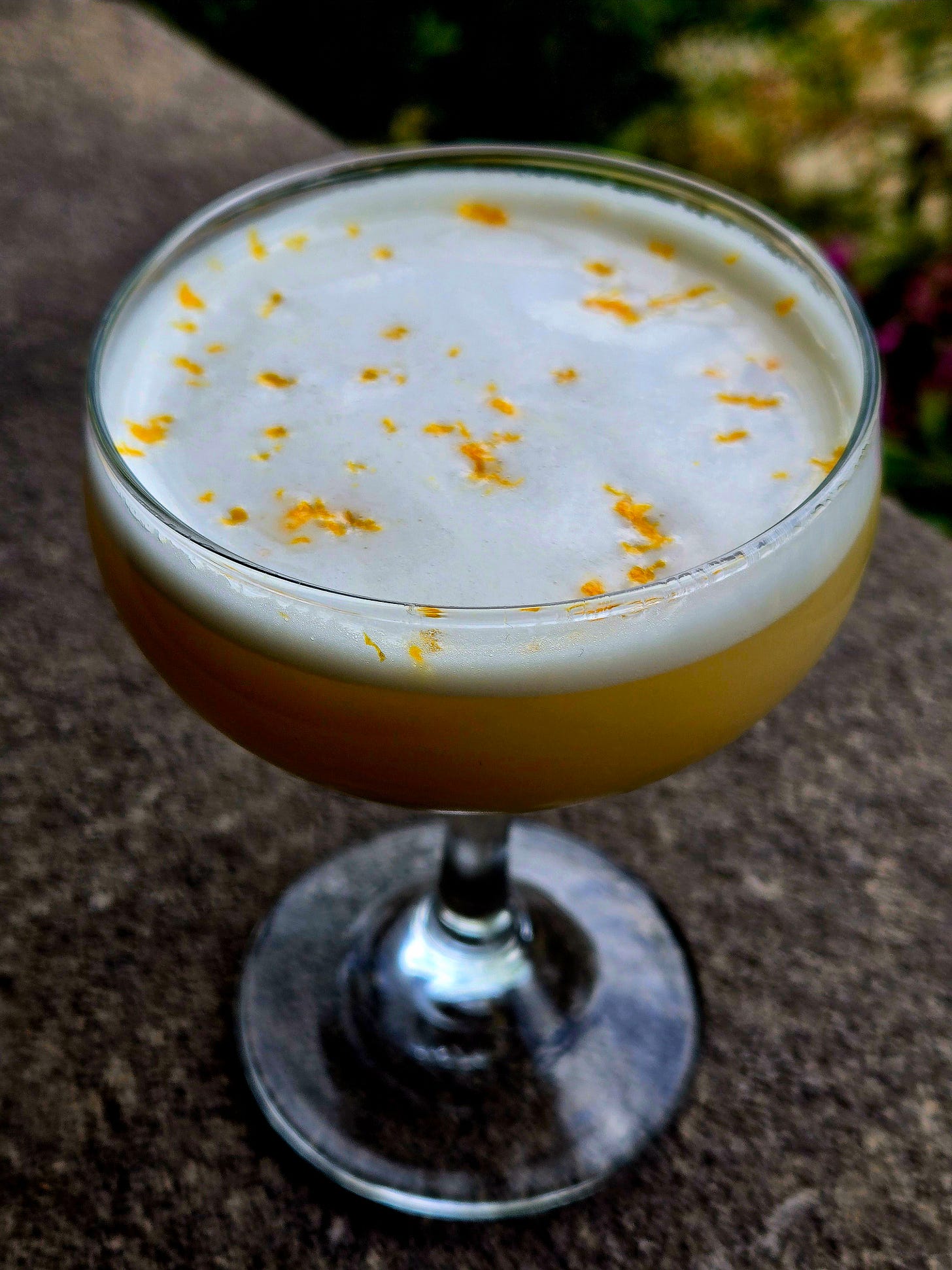 Beantown Bourbon in a Coupe with orange zest garnish atop a stone wall. Beantown Bourbon in a Coupe with orange zest garnish atop a stone wall.