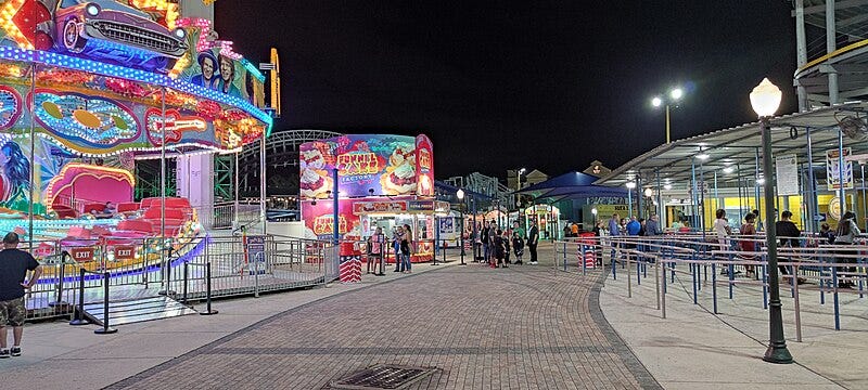 A brightly colored carousel and "Funnel Cake Factory"  sign in a nearly empty amusement park.