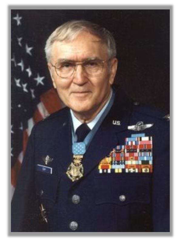 Headshot of Day, in uniform. He is wearing his Medal and there is an American flag in the background.