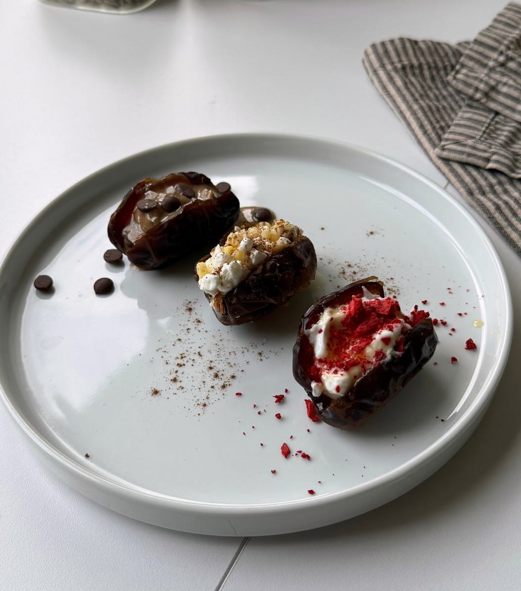 “Three Medjool dates stuffed with peanut butter, dark chocolate chips, and a sprinkle of sea salt on a white plate, a high-protein snack idea.”