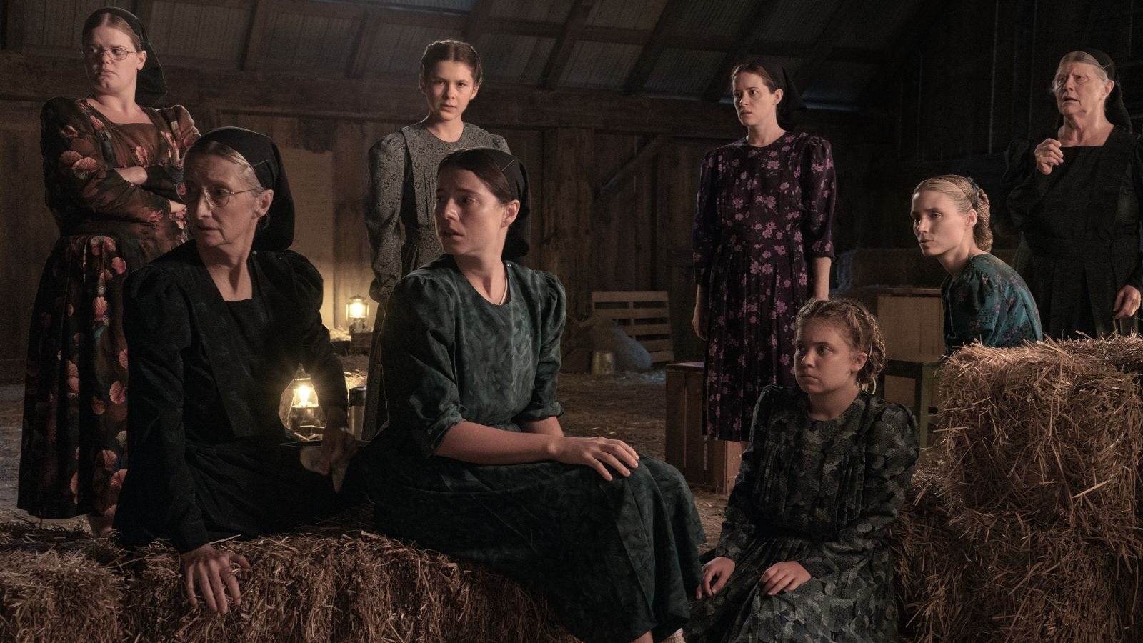 Seven Mennonite women and girls congregate in a hay barn.