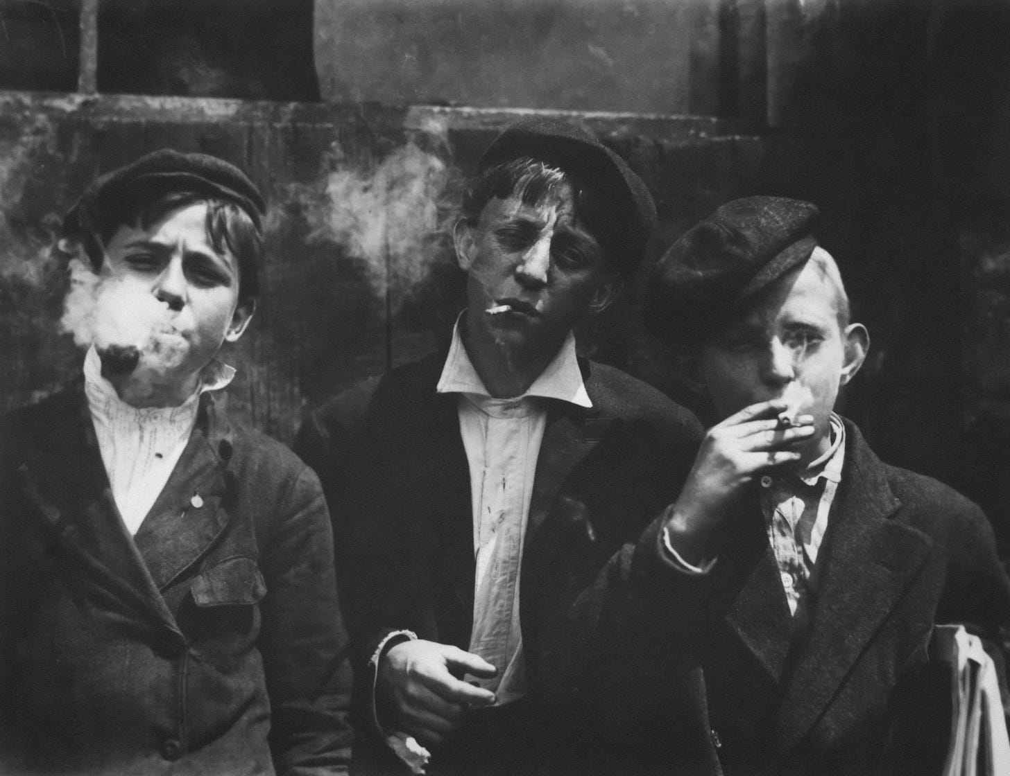 Vinatage black and white photo of three young boys smoking cigarettes and squinting at the camera.