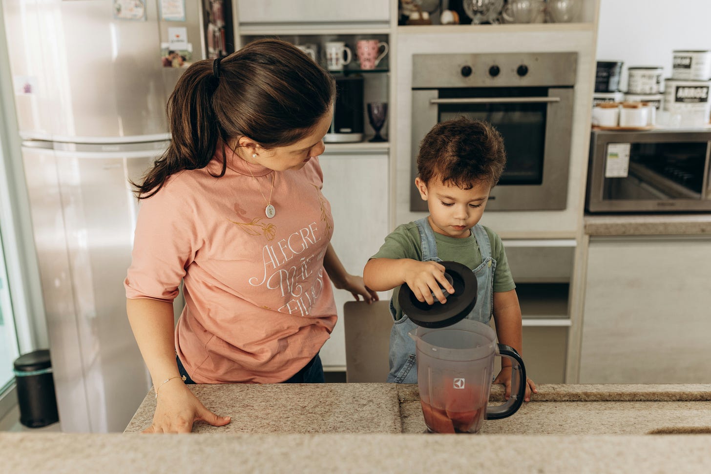 child and adult standing in a kitchen while child loads blender