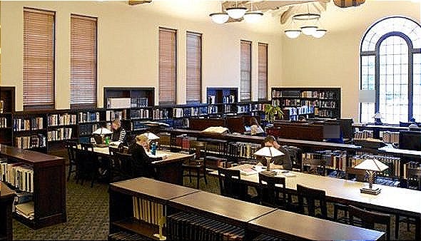 study room in the library - walls of bookshelves with long wooden desks that have small laps on them. A few people sitting at each table.