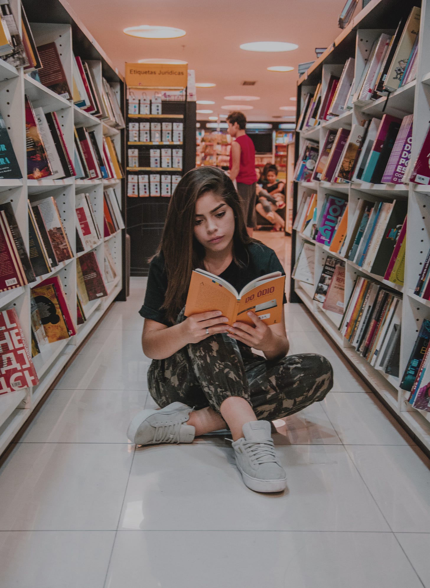 Young woman reading a book between two shelves of a bookshop